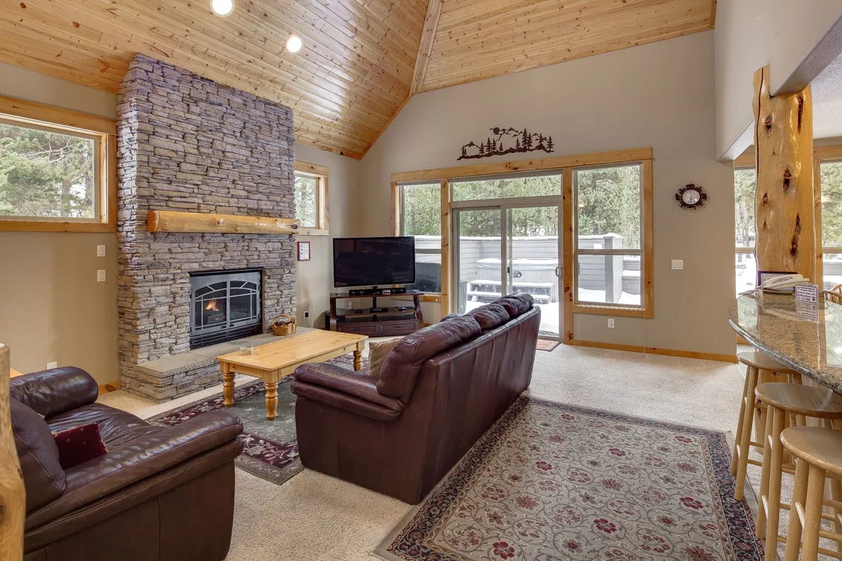 A welcoming living room anchored by a striking stone fireplace and large windows. Comfortable sofas and a wooden coffee table create a relaxed environment for family gatherings, movie nights, and enjoying the view.