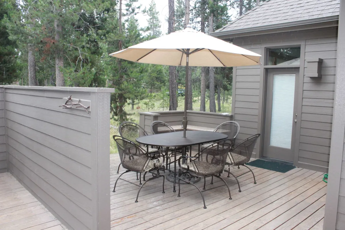 A serene outdoor dining area on a wooden deck, featuring a round table with an umbrella and wrought iron chairs. The setting is ideal for sharing stories, relaxing after games, or enjoying a meal together in the fresh air.