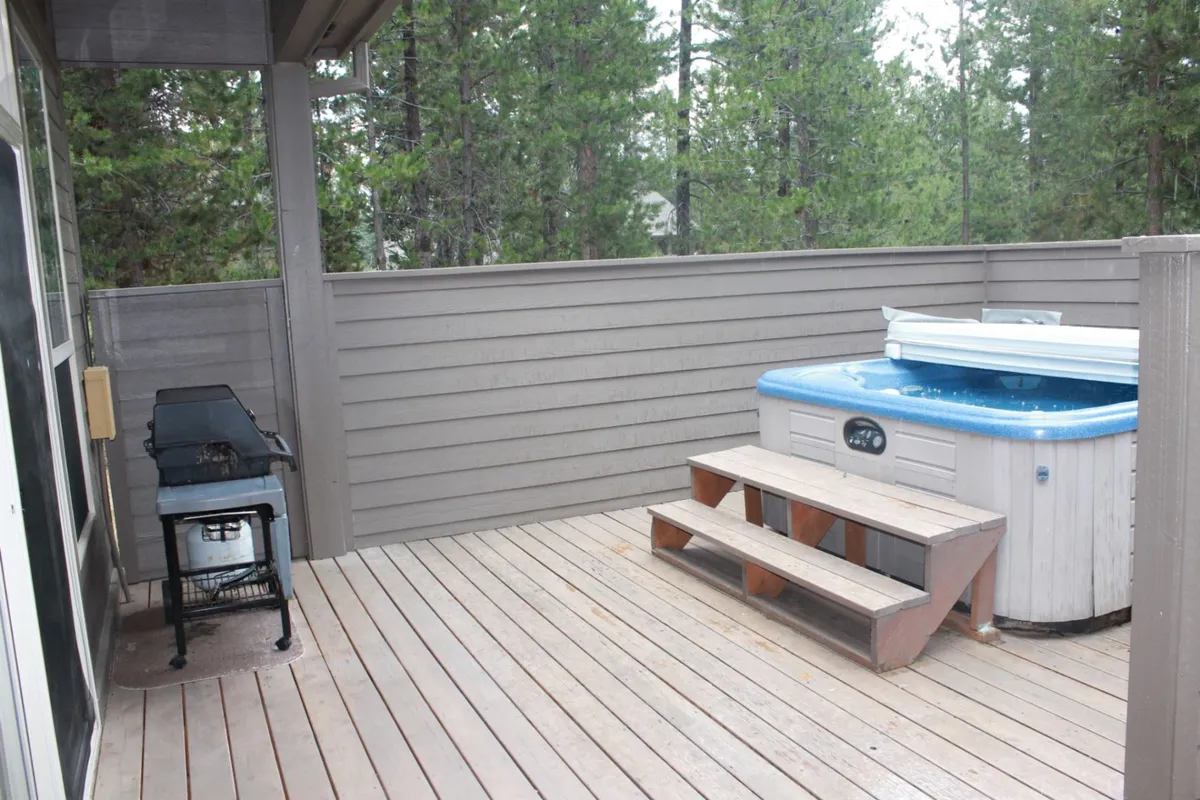 This exterior image features a private hot tub set on a wooden deck, accompanied by a grill and surrounded by natural trees. The atmosphere is serene, ideal for relaxation and outdoor gatherings, with clear cues that the space is both inviting and designed for enjoyment in any season.