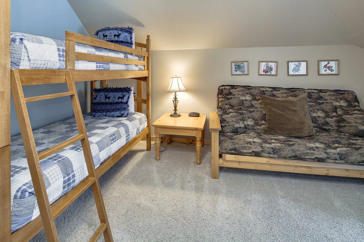 A playful bunk room designed for families or groups, featuring built-in bunk beds, a comfy sofa, a table lamp, and framed pictures on the walls. The space feels warm, fun, and welcoming—perfect for kids or multiple guests.