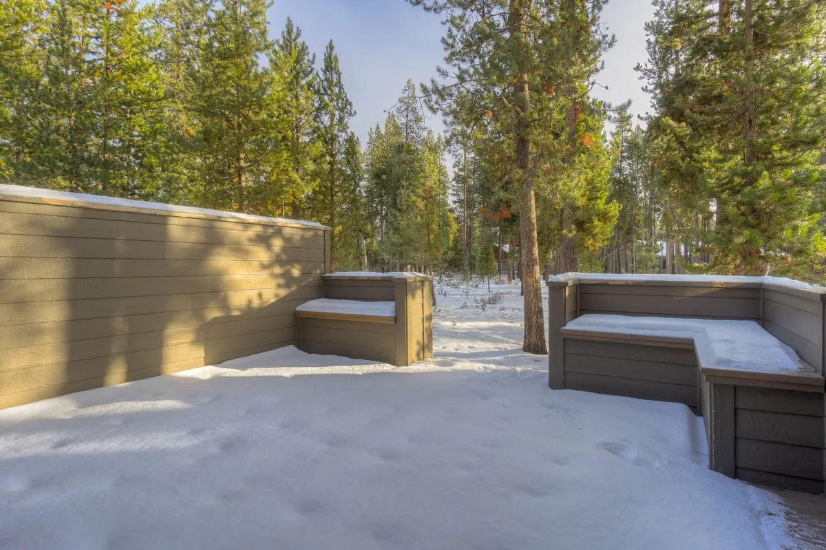 A peaceful outdoor scene featuring wooden seating areas nestled among tall pine trees on snow-covered ground. The space offers a tranquil spot for enjoying the outdoors, whether for reading, stargazing, or simply soaking in the scenery.