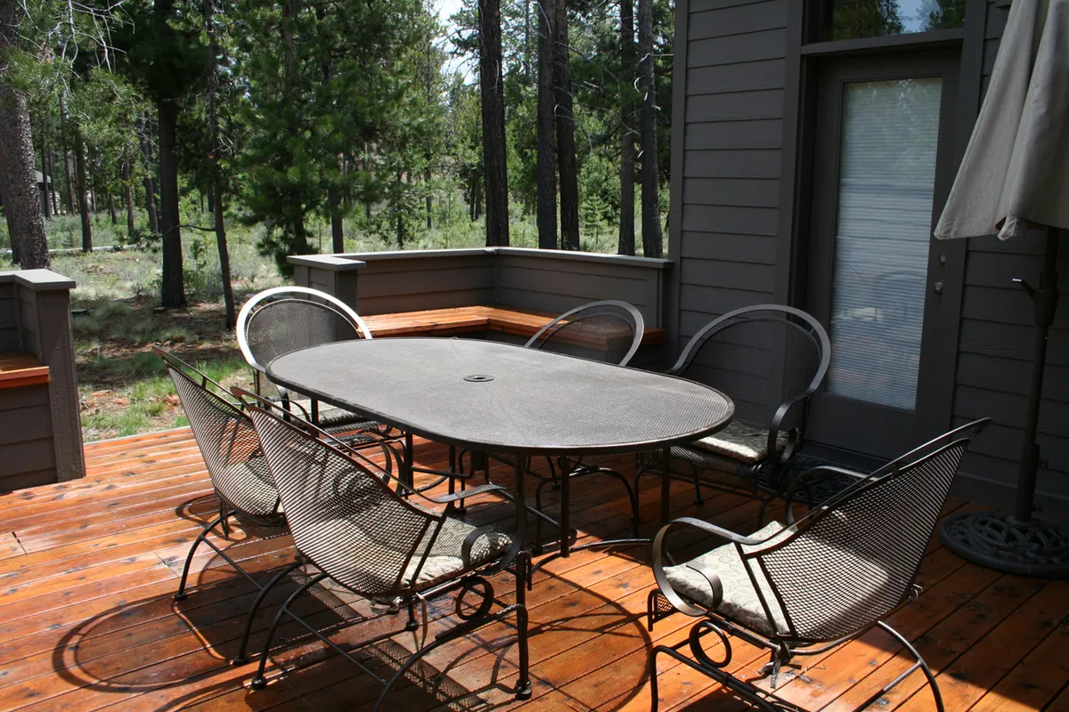An inviting wooden deck nestled among trees, featuring a round dining table with metal chairs. The tranquil setting is perfect for outdoor meals, morning coffee, or evening stargazing, and creates a seamless transition between indoor fun and the natural surroundings.