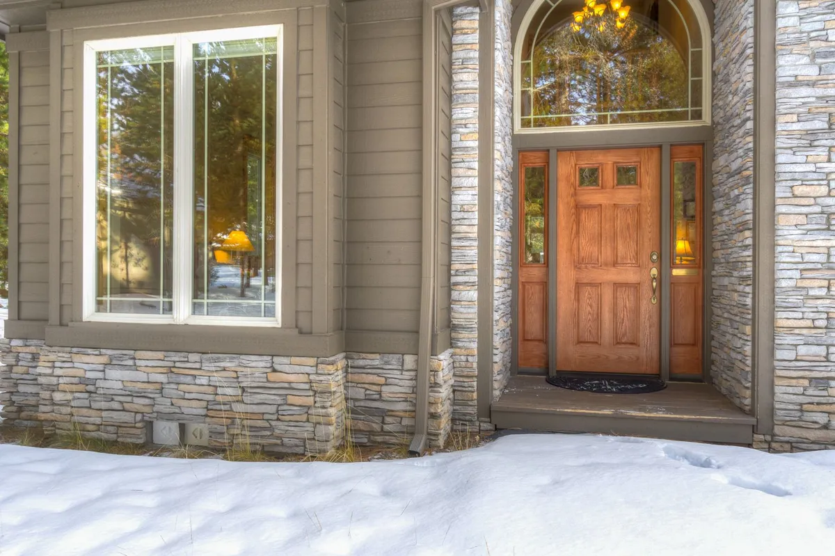 A welcoming view of the home's wooden front door and stone exterior, framed by large windows that hint at the cozy, communal atmosphere inside. The image evokes arrival and anticipation for group experiences within.